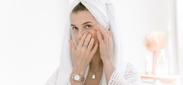 Kobieta w ręczniku wykonuje masaż twarzy