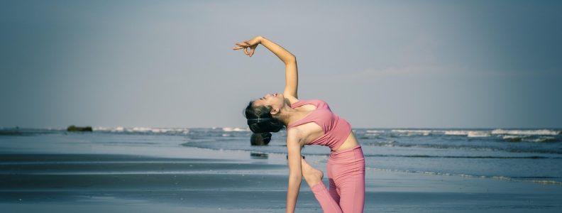 Kobieta wykonuje skłon kręgosłupa w pozycji klęczącej na macie na plaży